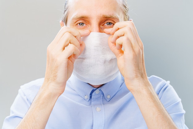 Homem barbudo branco de camisa azul coloca uma máscara de poluição do ar e coronavírus Covid-19.