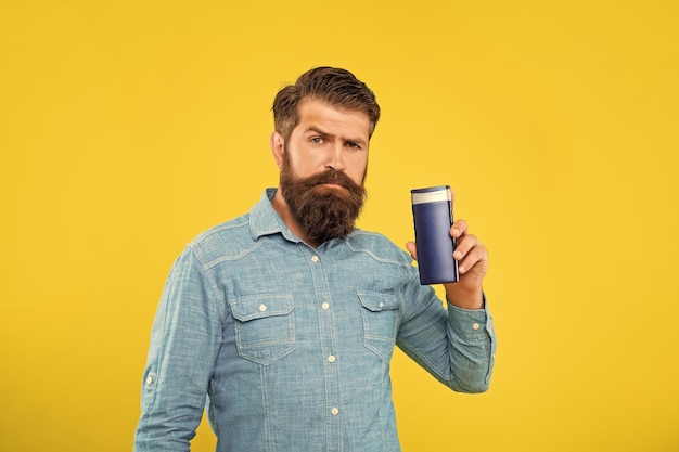 Homem barbudo brutal mostrando garrafa de condicionador de cabelo em fundo amarelo apresentando produtos de higiene pessoal