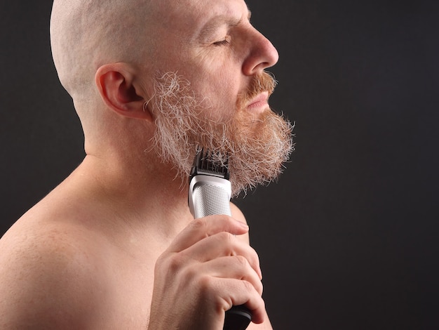 Homem barbudo com aparador para ajustar a barba na mão