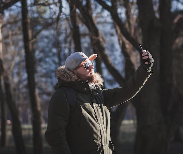 Homem barbudo com boné tirando uma selfie no parque