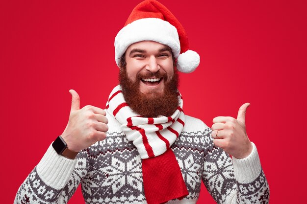 Homem barbudo com chapéu de natal sorrindo e mostrando o polegar