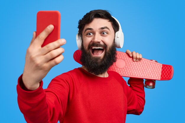Homem barbudo com longboard tirando selfie
