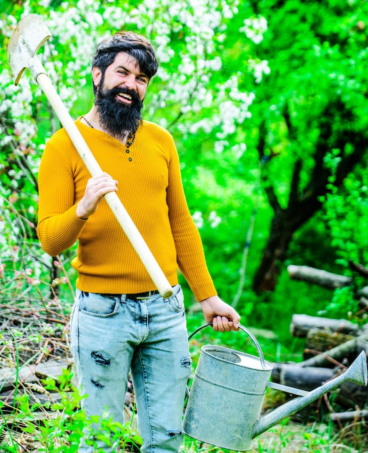 Foto homem barbudo com regador e pá agricultor trabalhando no jardim jardineiro trabalho jardinagem primavera