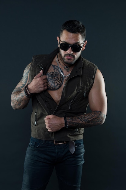 Homem barbudo com tatuagem no peito e braços Estilo de moda e tendência Modelo de tatuagem com barba no rosto por barbear Homem tatuado com bíceps e tríceps Moda macho em óculos de sol da moda