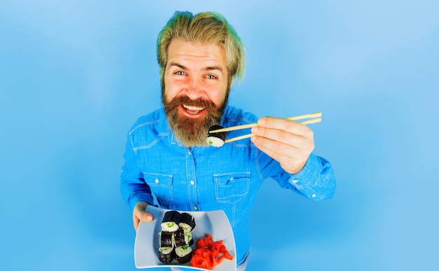 Homem barbudo come sushi roll cara bonito com gengibre em conserva e sushi roll no prato comida japonesa