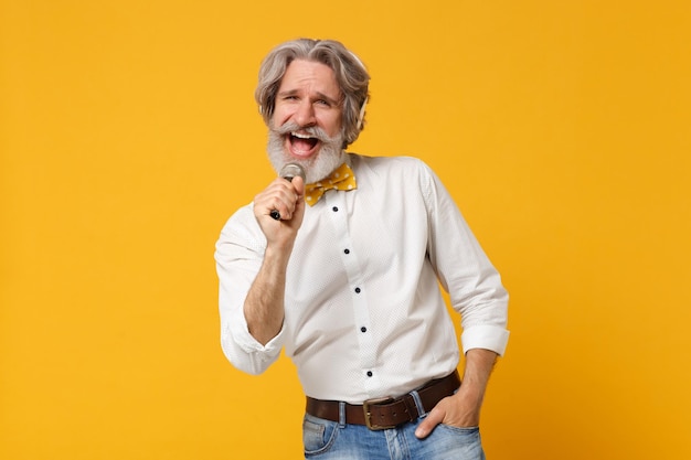 Homem barbudo de bigode grisalho idoso alegre em gravata borboleta de camisa isolada em fundo amarelo. Conceito de estilo de vida de pessoas. Mock up espaço de cópia. Ouça música com fones de ouvido, cante música no microfone.