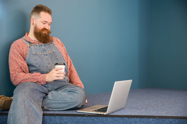 Homem barbudo de macacão azul tomando café