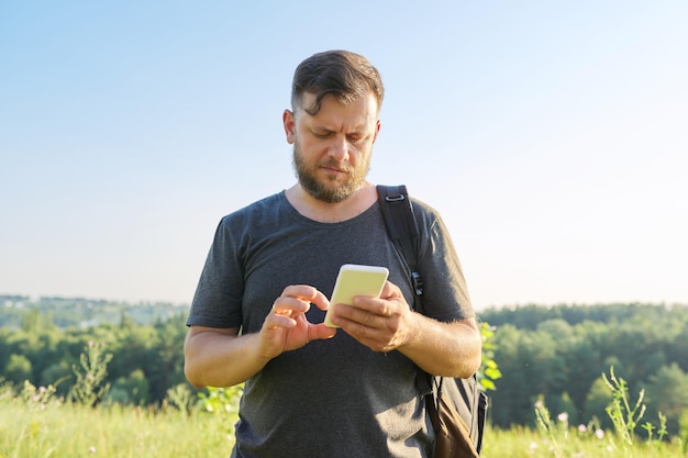 Homem barbudo de meia idade com mochila usando smartphone