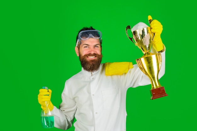 Homem barbudo de uniforme e luvas com spray de limpeza e copa troféu de ouro profissional