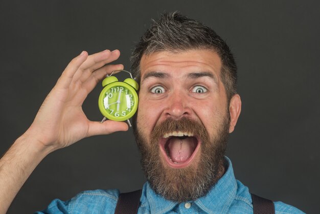 Homem barbudo e sorridente com despertador no fundo preto macho segurando o despertador perto do rosto feliz