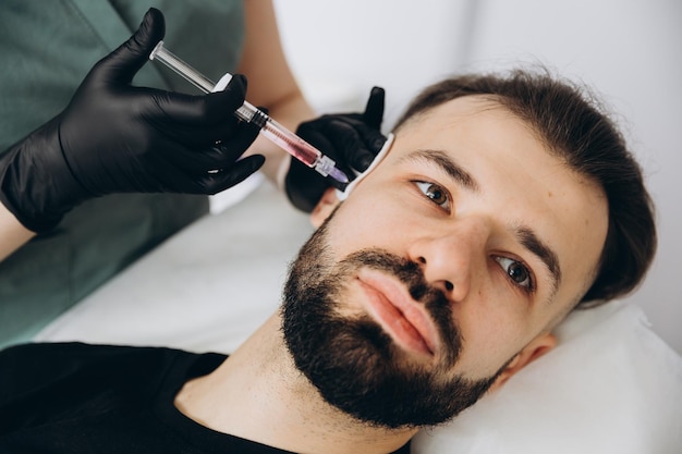 Homem barbudo elegante visitando clínica estética recebendo preenchimento de lábios closeup Homem atraente tendo injeção de beleza no salão de spa masculino Tratamento antienvelhecimento para homens conceptxD