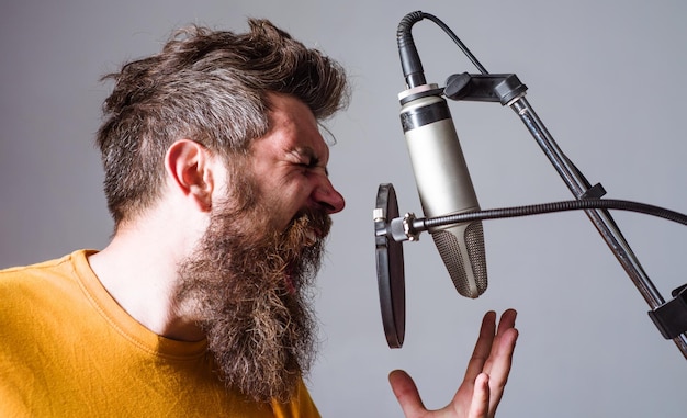 Homem barbudo em cara de karaokê cantando no microfone condensador vocalista profissional em registros de estúdio