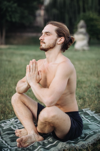 Homem barbudo em pose de lótus, sentado na grama verde, conceito de calma e meditação