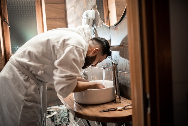 Homem barbudo em um roupão de banho no banheiro. Noivo de manhã, prepare-se para o casamento no hotel. Foto de moda de um homem.