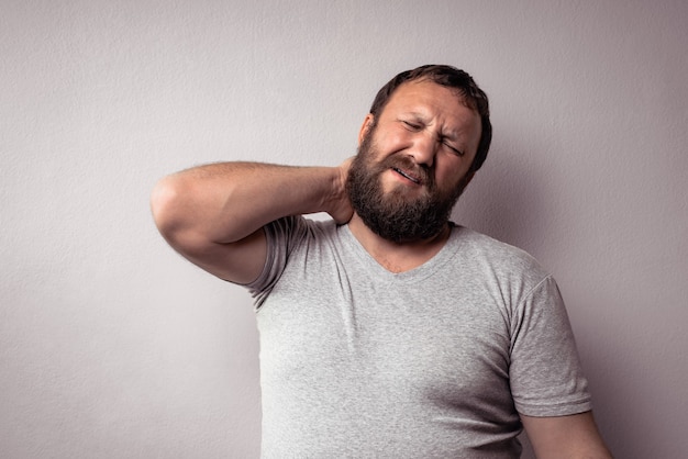 Homem barbudo em uma camiseta cinza se sentindo exausto e segurando seu pescoço parecendo exausto