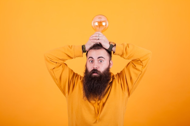 Homem barbudo engraçado com uma lâmpada na cabeça na frente sobre fundo amarelo. Ótima mente. Homem inteligente. Ótima solução