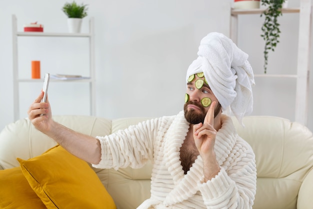 Homem barbudo engraçado segurando fatias de pepino no rosto. spa em casa, corpo e pele para o conceito masculino.