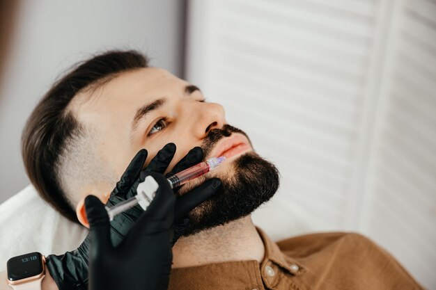 Homem barbudo estiloso visitando clínica estética recebendo preenchimento labial fechado