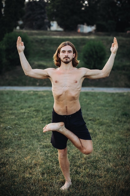 Homem barbudo fazendo yoga no parque verde