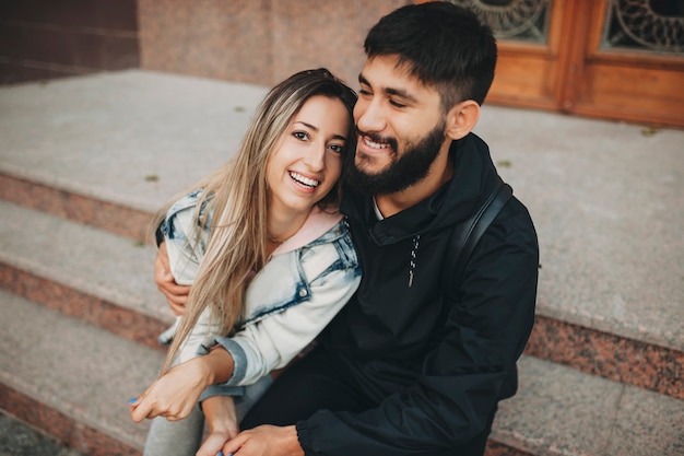 Foto homem barbudo feliz e mulher alegre se abraçando enquanto está sentado nos degraus da rua