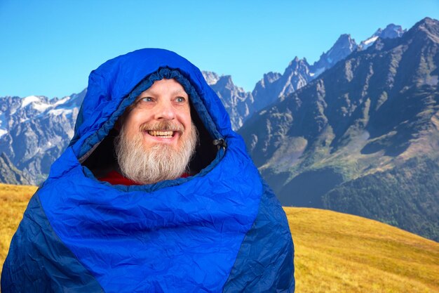 Homem barbudo feliz em um saco de dormir contra o pano de fundo da natureza nas montanhas