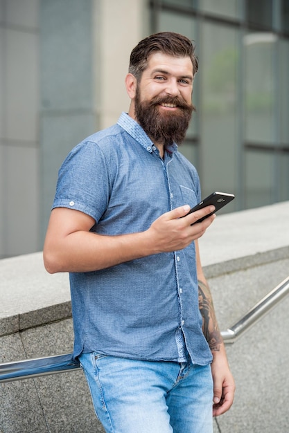 Homem barbudo feliz sorrindo usando celular dispositivo móvel ao ar livre celular