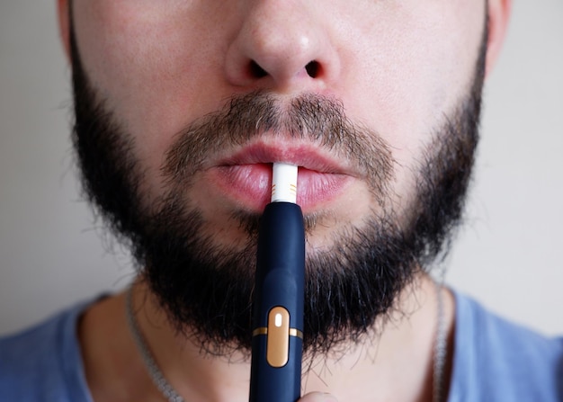 Homem barbudo fuma um cigarro eletrônico closeup