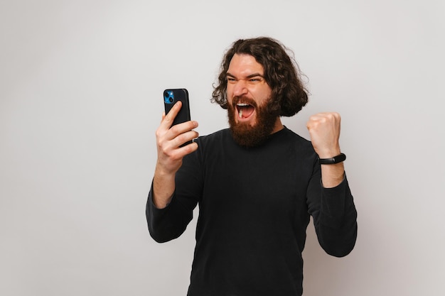 Homem barbudo grita enquanto olha para o telefone e faz o gesto de vencedor