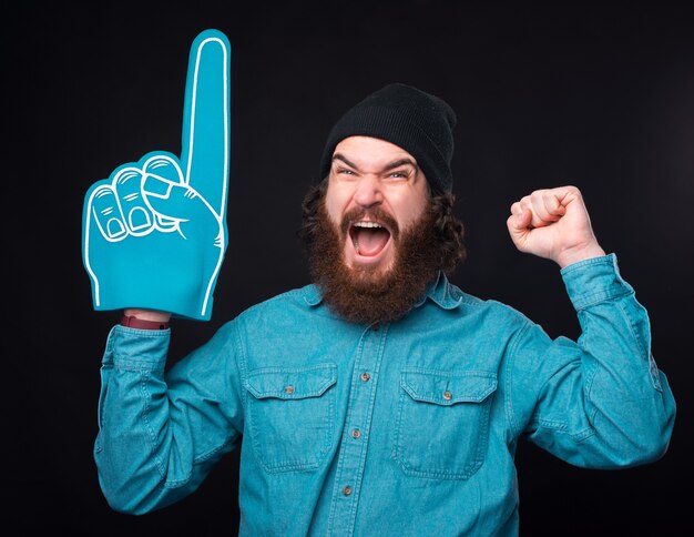 Homem barbudo hippie espantado apontando com uma luva em leque e comemorando a vitória do time favorito