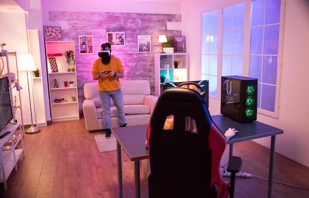 Foto homem barbudo jogando usando óculos vr, enquanto sua garota está jogando jogos de tiro no computador. cadeira de jogos. luz neon.