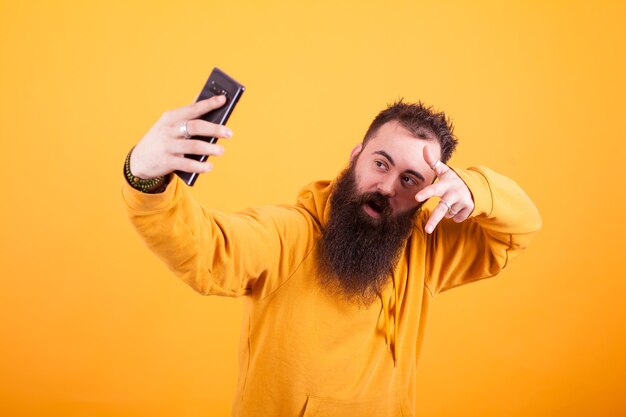 Homem barbudo legal vestindo moletom amarelo e tomando selfie sobre fundo amarelo. Homem moderno. Homem Stylysh,