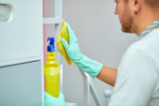 Foto homem barbudo limpando a superfície da mesa em casa com toalha e luvas, frasco de spray desinfetante, quebrando estereótipos de gênero, gênero neutro.