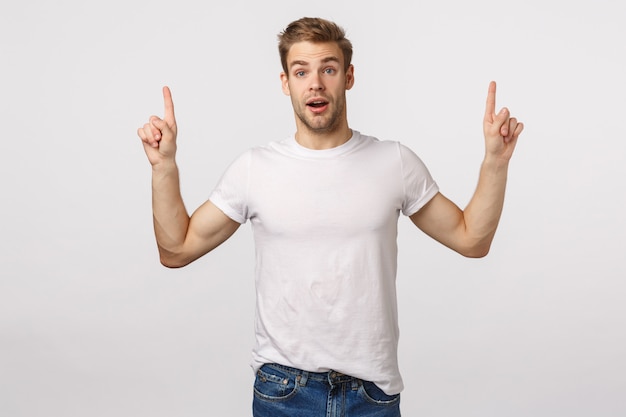 Homem barbudo loiro atraente em camiseta branca apontando para cima