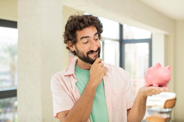 Foto homem barbudo louco sorrindo com uma expressão feliz e confiante com a mão no queixo conceito de cofrinho