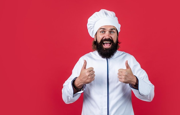 Homem barbudo maduro usa chapéu de chef cozinheiro masculino pronto para preparar comida hipster brutal no avental vai cozinhar a hora da refeição para comer o conceito de cozimento feliz de limpeza polegar para o sucesso