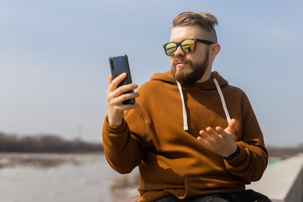 Homem barbudo milenar fazendo videochamada no celular ao ar livre no smartphone de videochamada da cidade e