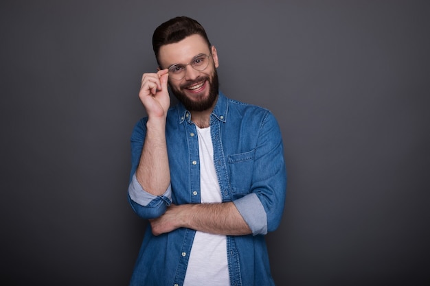 Homem barbudo moderno inteligente e confiante em roupas jeans casuais e óculos posando