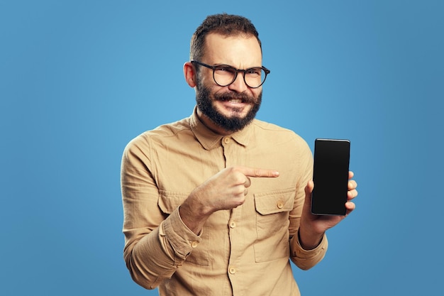 Homem barbudo mostrando celular com tela em branco isolado sobre fundo azul