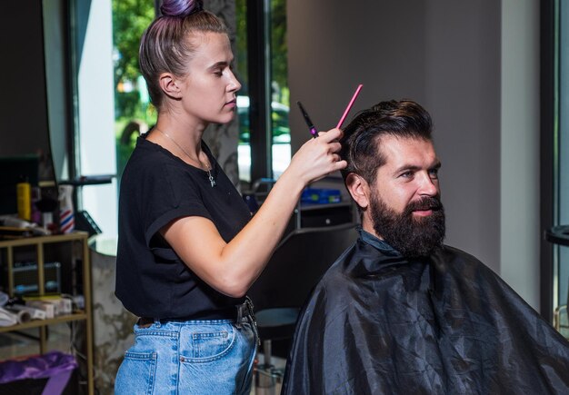 Homem barbudo na cadeira de cabeleireiro no salão de beleza e moda cabelo e barba estilo brutal com mestre profissional de barbearia use barbeador elétrico Pronto para barbear matinal cuidados de barbeiro masculino