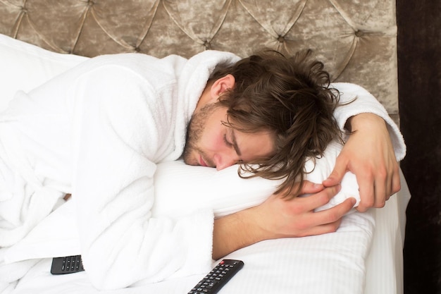 Homem barbudo na cama com controle remoto