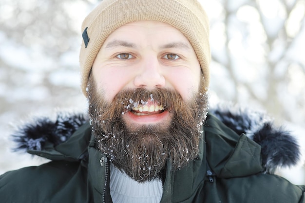 Homem barbudo na floresta de inverno. Jovem feliz atraente com barba andar no parque.