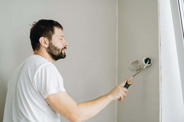 homem barbudo pintando parede com rolo de tinta Pintando apartamento reformando casa com tinta cinza