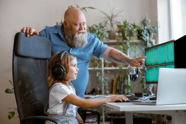 Homem barbudo positivo ensina filha a trabalhar com um programa de computador no local de trabalho