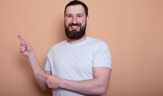 Homem barbudo positivo vestindo camiseta indicando à venda espaço vazio isolado em fundo de cor bege