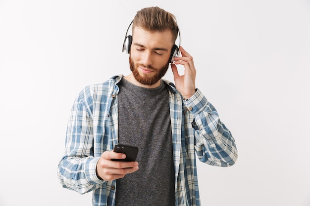 Homem barbudo satisfeito com camisa e fones de ouvido ouvindo música