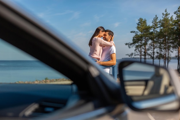 Homem barbudo segurando namorada nas mãos com carro em primeiro plano