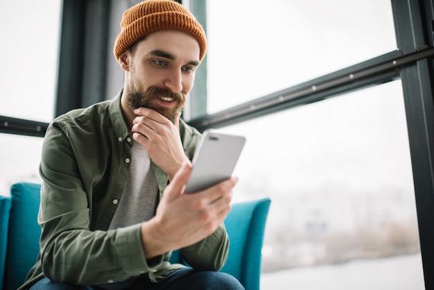 Homem barbudo segurando o celular, comunicação, reserva de bilhetes, assistindo filme, sentado no café moderno.