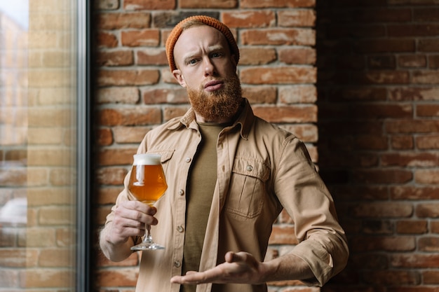 Homem barbudo segurando o copo de cerveja, bebendo álcool no pub
