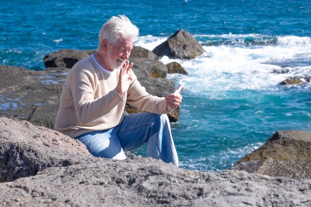 Homem barbudo sênior, apreciando a excursão no mar, sentado usando um telefone celular. Horizonte sobre a água