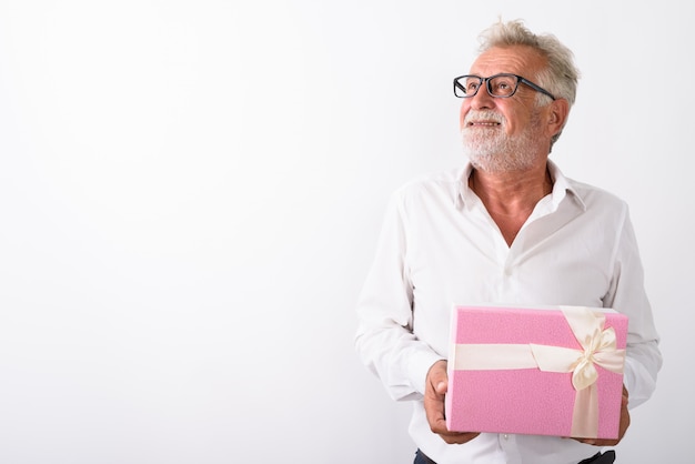 homem barbudo sênior feliz sorrindo e pensando, segurando uma caixa de presente com óculos em branco